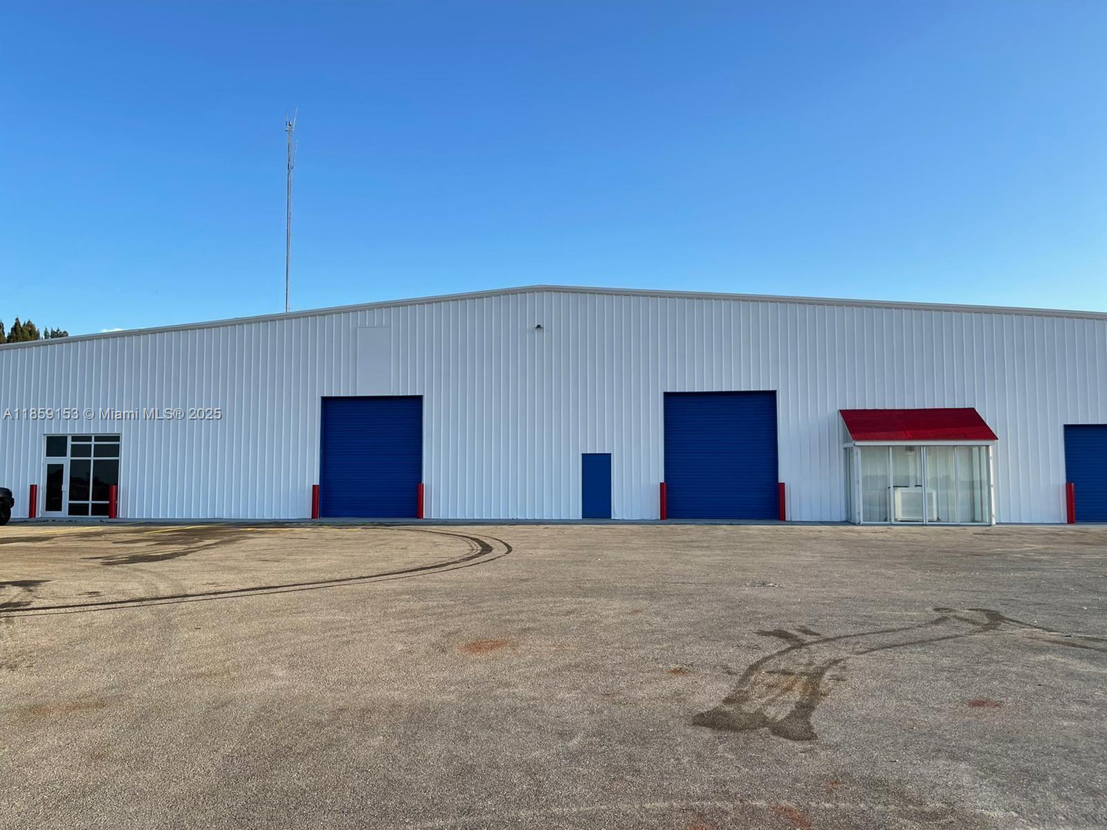 The exterior of a white industrial warehouse building features blue roll-up doors and a red awning — 14961 SR W78, Moore Haven FL 33471, MOORE HAVEN, FL