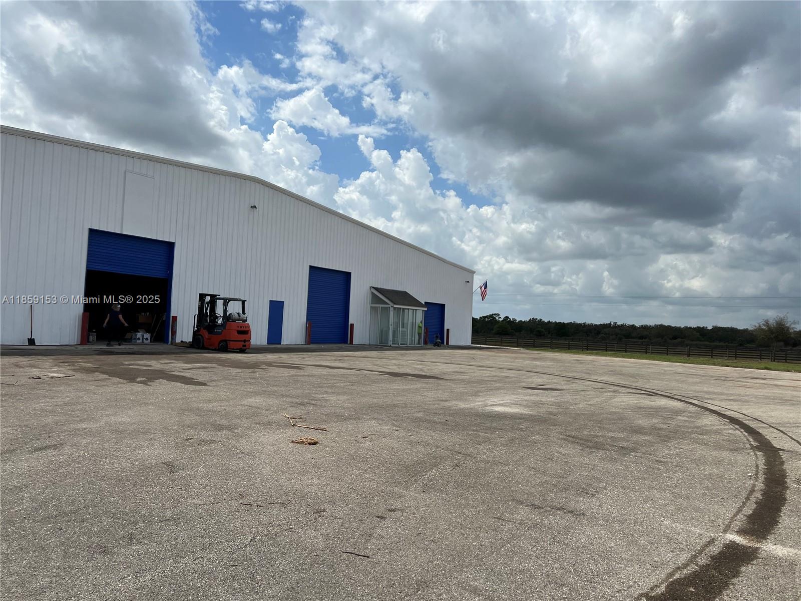 A large white industrial warehouse building features blue roll-up doors and a paved parking lot — 14961 SR W78, Moore Haven FL 33471, MOORE HAVEN, FL