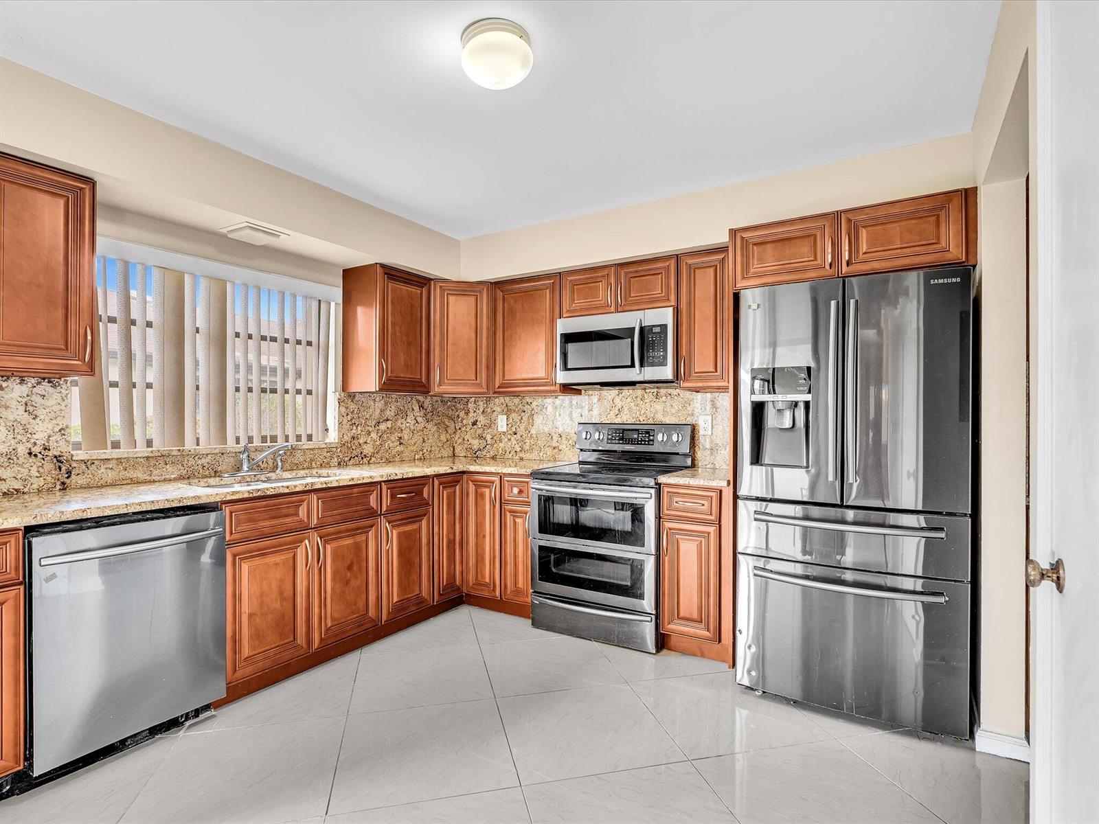 A kitchen features wood cabinets, granite countertops, stainless steel appliances, and light-colored tile flooring — 4951 Equestrian Circle # A, Boynton Beach FL 33436, BOYNTON BEACH, FL