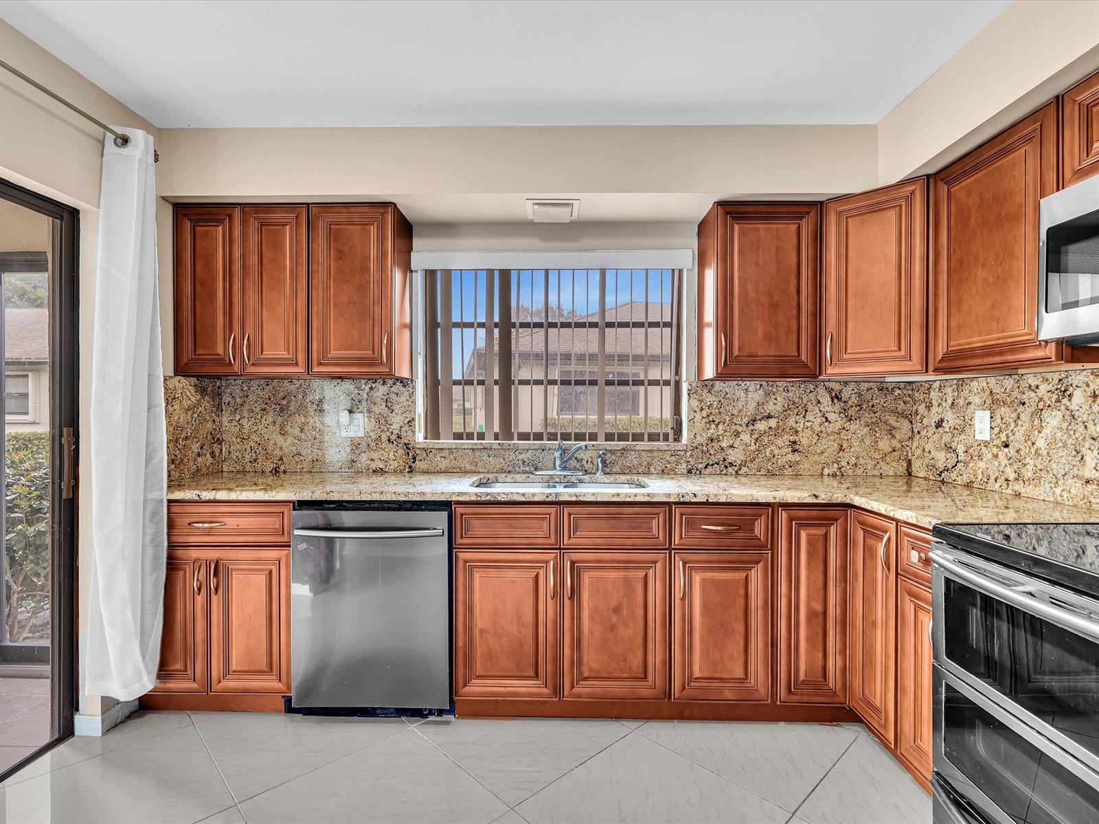 A kitchen features wood cabinets, granite countertops, a stainless steel dishwasher, and a window view — 4951 Equestrian Circle # A, Boynton Beach FL 33436, BOYNTON BEACH, FL