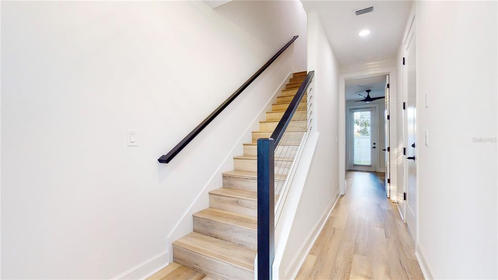 A staircase with light wood steps and a black railing leads upward in a hallway — 1520 N PIERCE STREET UNIT 5, TAMPA, FL