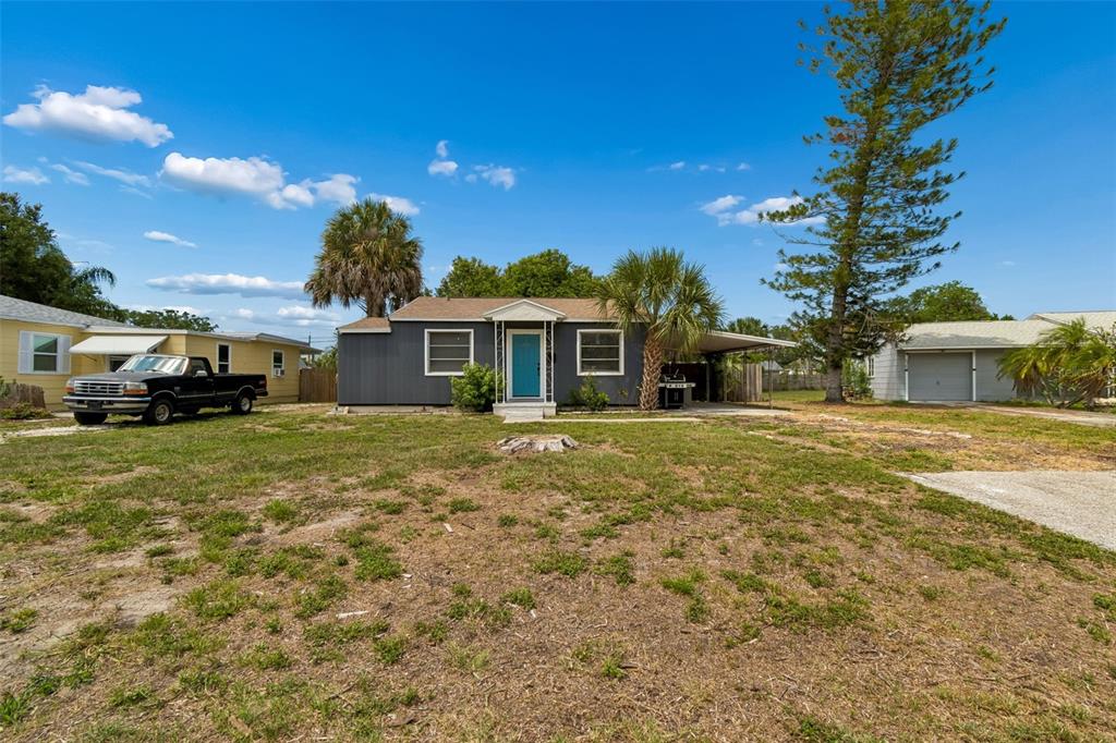 A gray, single-story house with a teal front door sits on a large, grassy lot — 517 HAMPTON AVENUE NE, ST PETERSBURG, FL