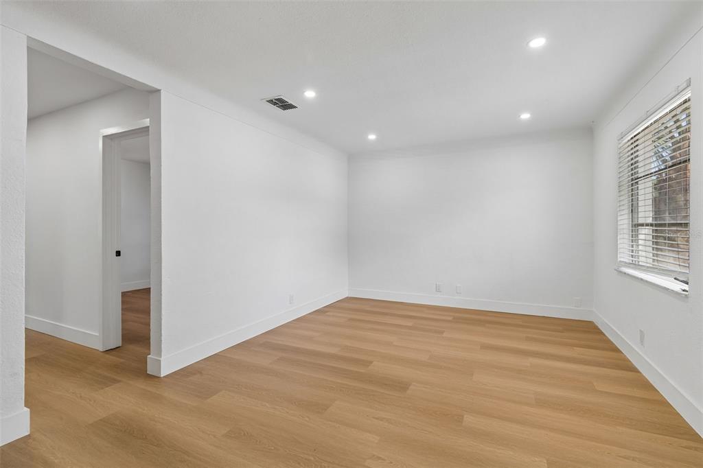An empty room features white walls, light wood-look flooring, recessed lighting, and a window — 517 HAMPTON AVENUE NE, ST PETERSBURG, FL