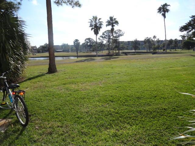 A bicycle sits on a grassy lawn overlooking a pond and palm trees — 3593 Birdie Drive # 103, FL 33467, FL