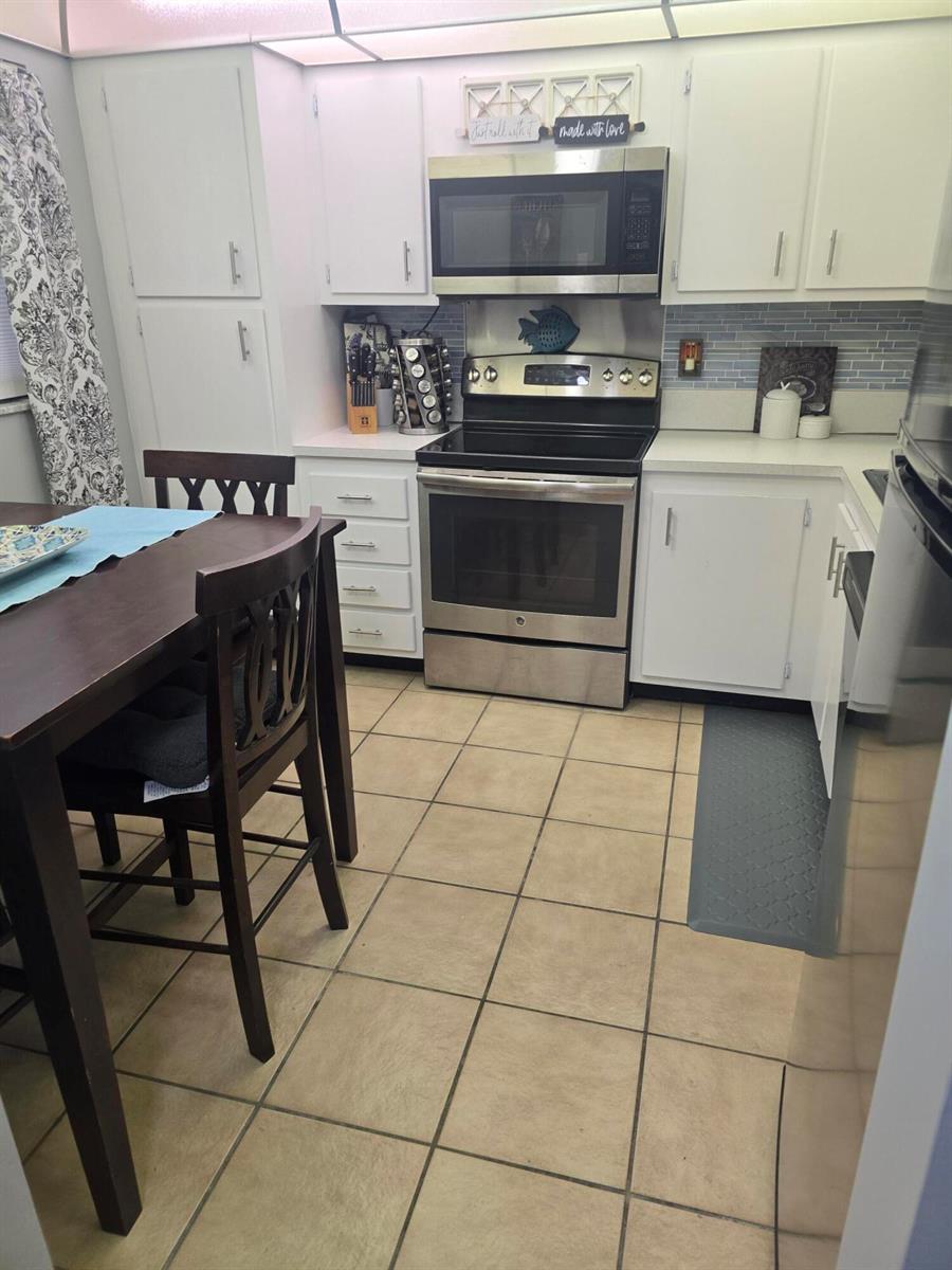 A kitchen features white cabinets, stainless steel appliances, a tile floor, and a dining table — 3593 Birdie Drive # 103, FL 33467, FL