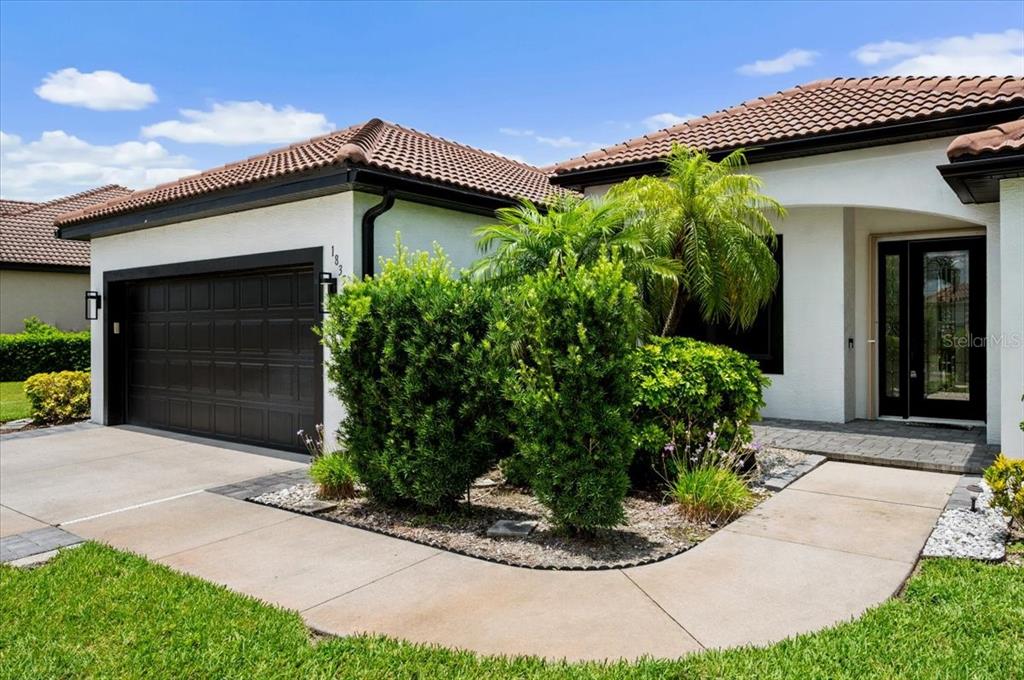 A single-story house exterior features a dark garage door, a palm tree, and landscaping — 1835 BOBCAT TRAIL, NORTH PORT, FL