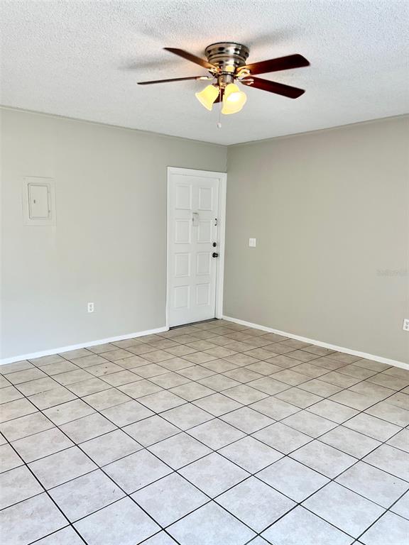An empty room features light-colored tile flooring, a ceiling fan, and a white entry door — 6065 VILLAGE CIRCLE UNIT 6065, ORLANDO, FL