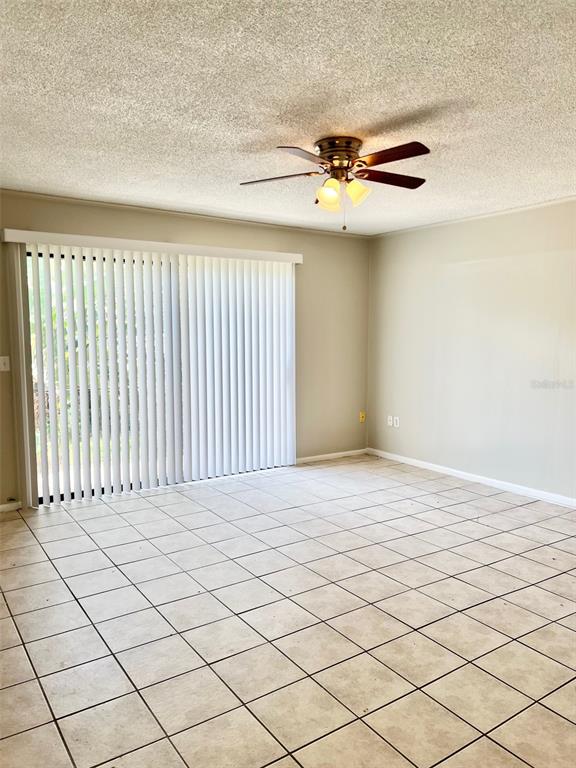 An empty room features light-colored floor tiles, a ceiling fan, and sliding glass patio doors — 6065 VILLAGE CIRCLE UNIT 6065, ORLANDO, FL