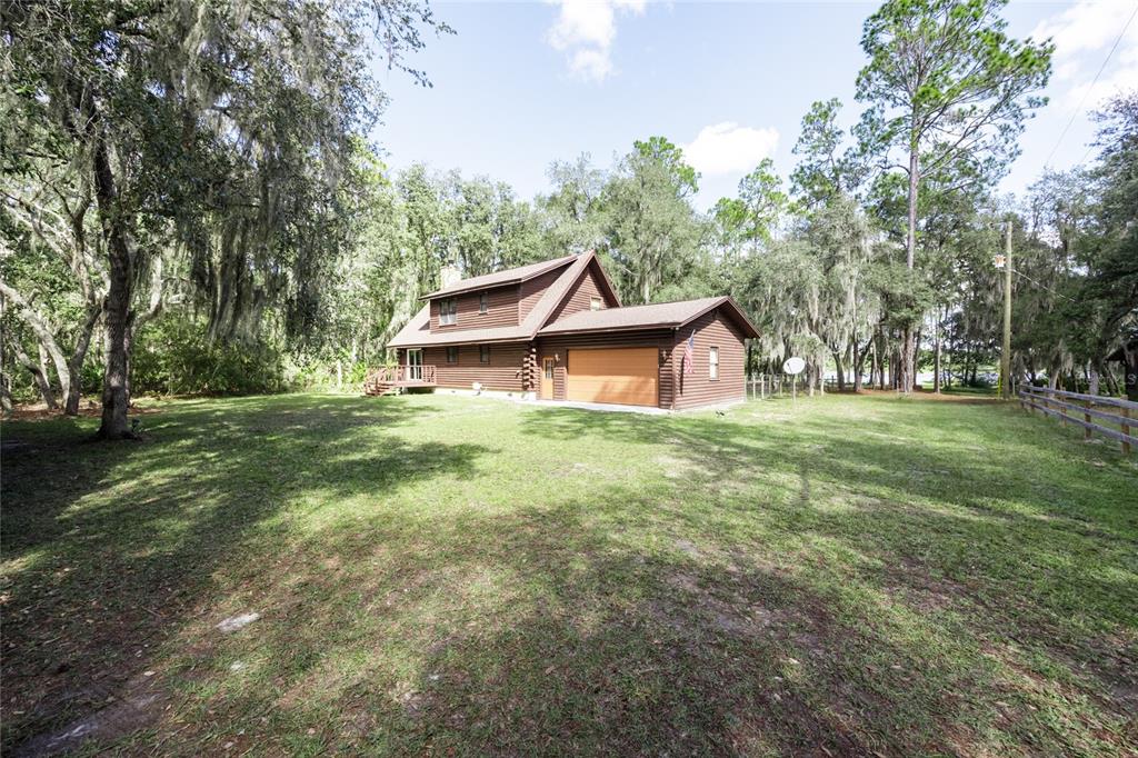 A two-story log cabin home with an attached garage sits on a large grassy lot — 239 RILEY LAKE DRIVE, HAWTHORNE, FL