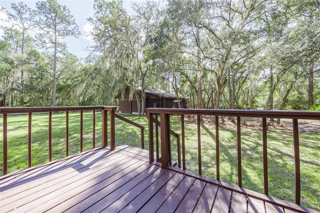 A wooden deck with railings overlooks a grassy yard and a small cabin among trees — 239 RILEY LAKE DRIVE, HAWTHORNE, FL