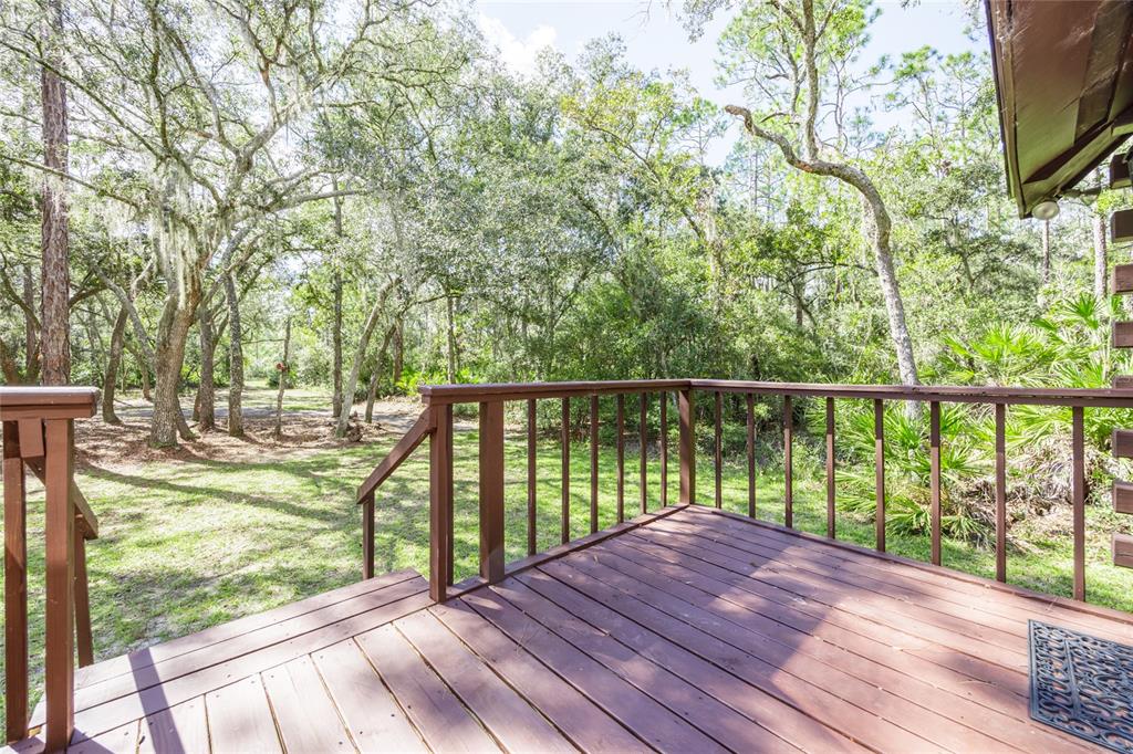 A wooden deck with railings overlooks a wooded backyard with trees and green foliage — 239 RILEY LAKE DRIVE, HAWTHORNE, FL