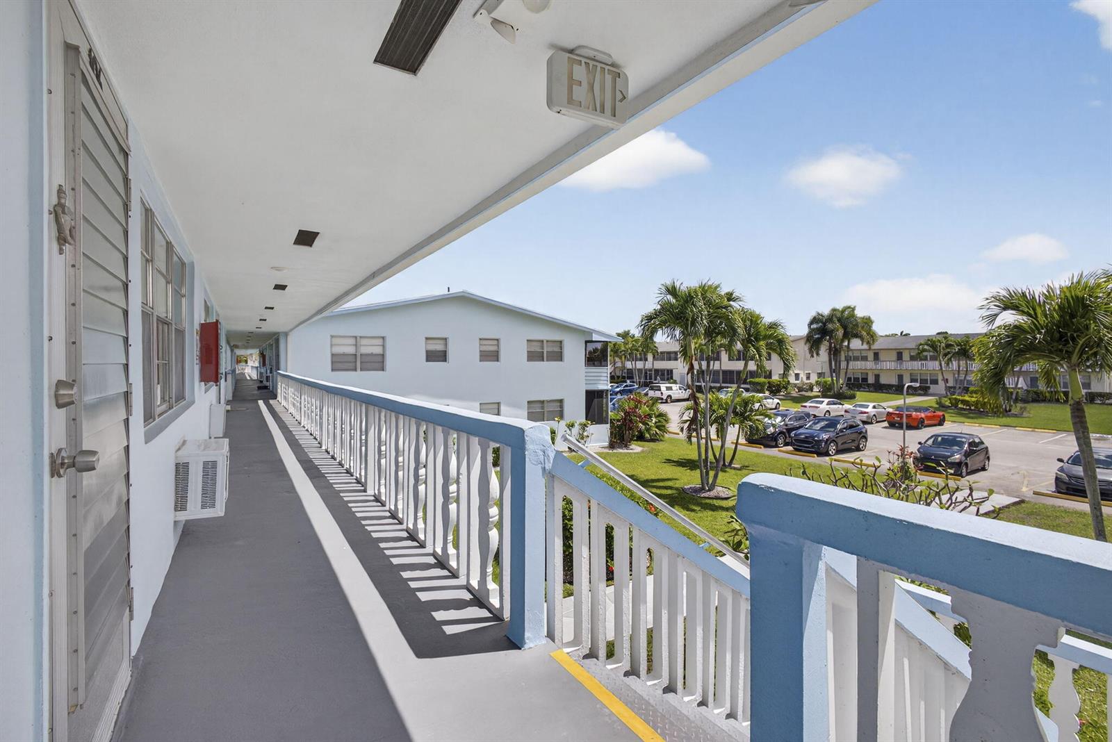 An outdoor apartment walkway overlooks a parking lot with palm trees and a blue sky — 106 E Camden E, West Palm Beach FL 33417, WEST PALM BEACH, FL