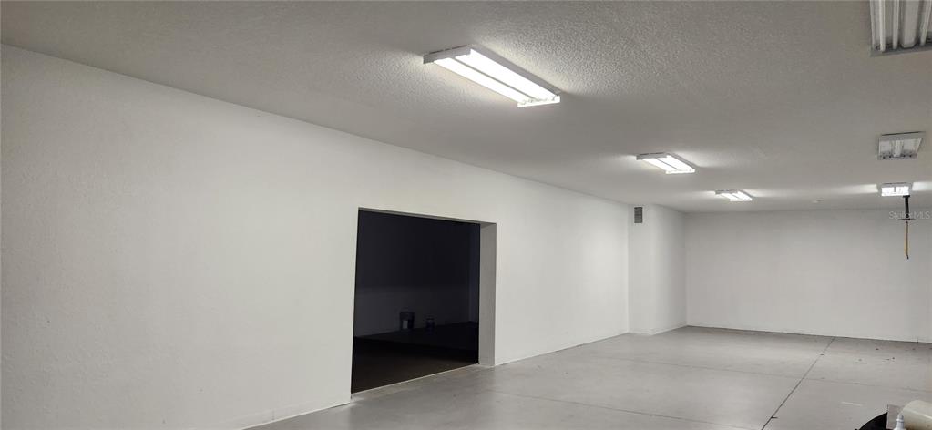 A spacious, white-walled garage with a concrete floor and multiple overhead fluorescent light fixtures — 610 N COMBEE ROAD, LAKELAND, FL