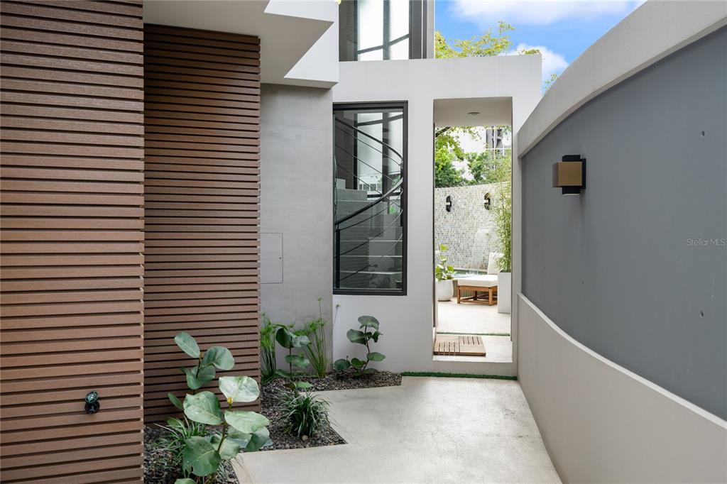 A modern outdoor walkway leads past a slatted wall toward a patio with a pool — 1 ALMENDARES, SAN JUAN, PR