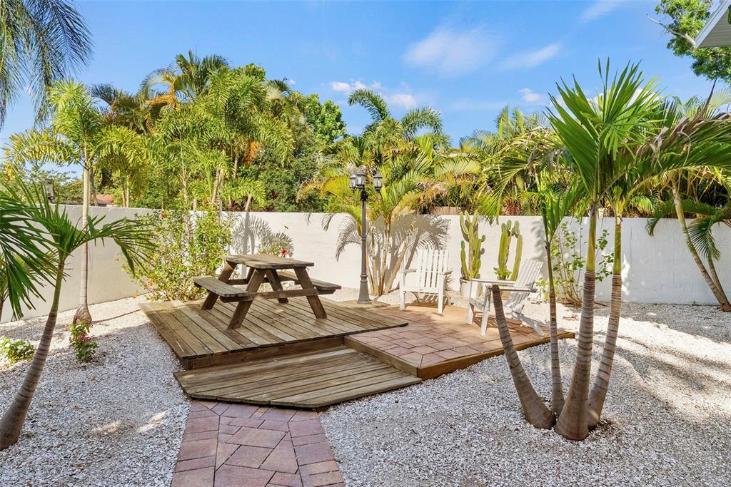 A backyard patio features a wooden picnic table, two white chairs, and a stone walkway — 3036 6TH AVENUE N, ST PETERSBURG, FL