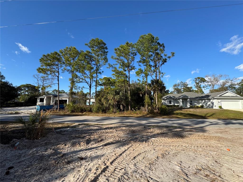 A vacant, sandy lot sits between two suburban houses under a clear blue sky — Lot 28 SWISS AVENUE, NORTH PORT, FL