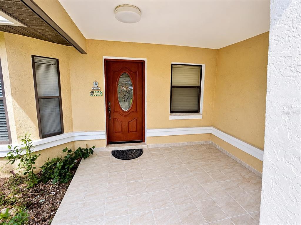 A tiled front porch features a wooden door with a glass oval insert and windows — 13506 SW 43RD CIRCLE SW, OCALA, FL