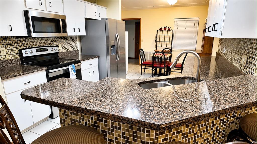 A kitchen features granite countertops, white cabinetry, a stainless steel refrigerator, and a tiled backsplash — 13506 SW 43RD CIRCLE SW, OCALA, FL