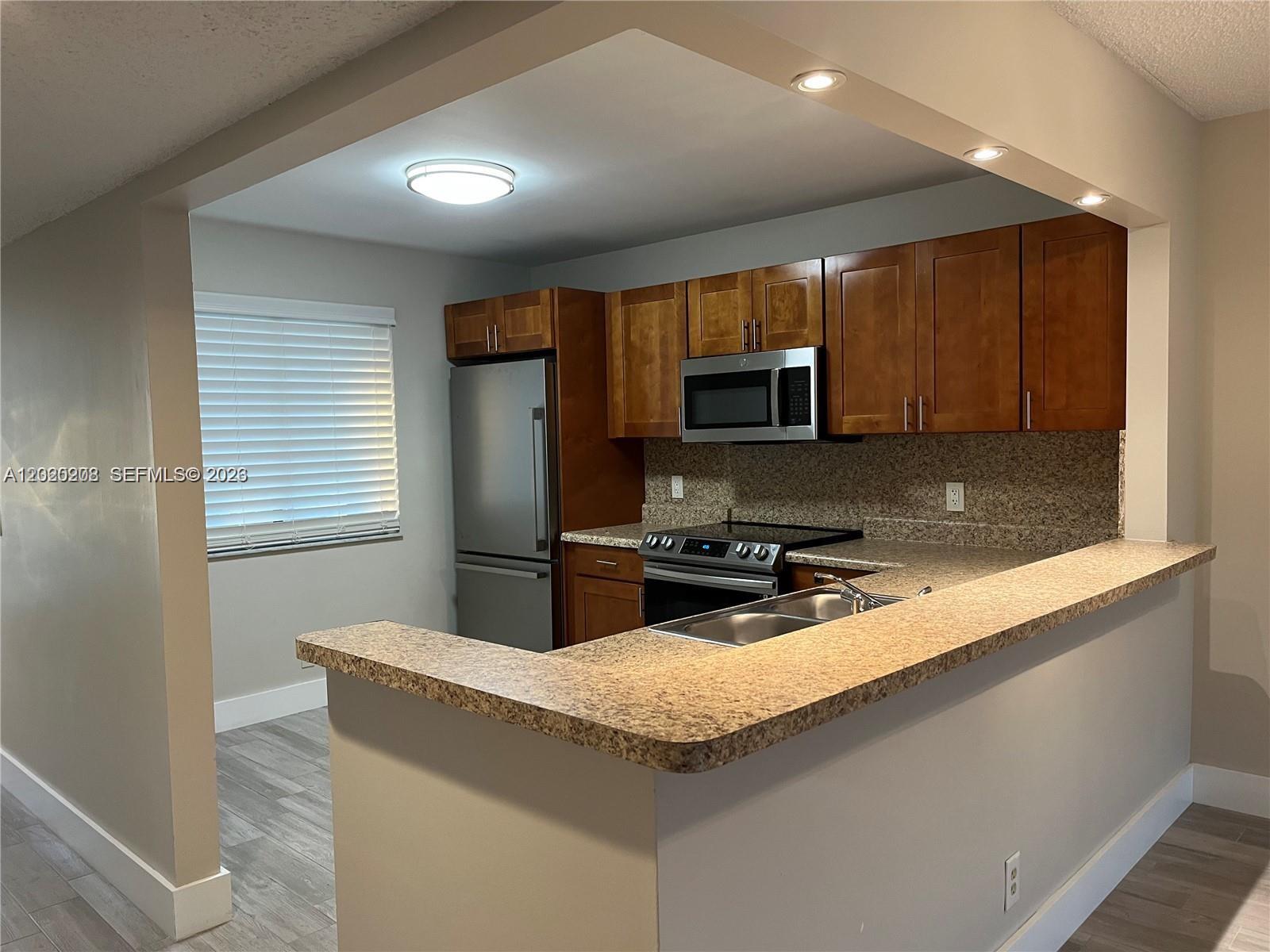 A kitchen features wood cabinets, stainless steel appliances, and a granite-topped breakfast bar — 436 Lakeview Dr # 203, Weston FL 33326, WESTON, FL