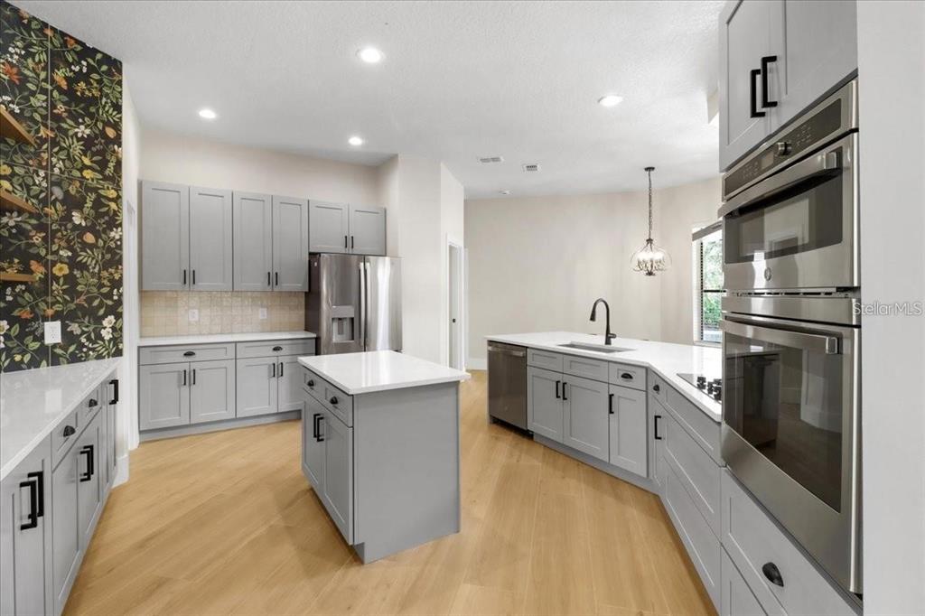 A modern kitchen features gray cabinets, white countertops, a center island, and floral wallpaper — 14024 CHERRY BUSH COURT, ORLANDO, FL