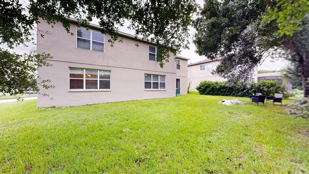 The exterior of a two-story beige house features a grassy backyard and several windows — 14796 TULLAMORE LOOP, WINTER GARDEN, FL