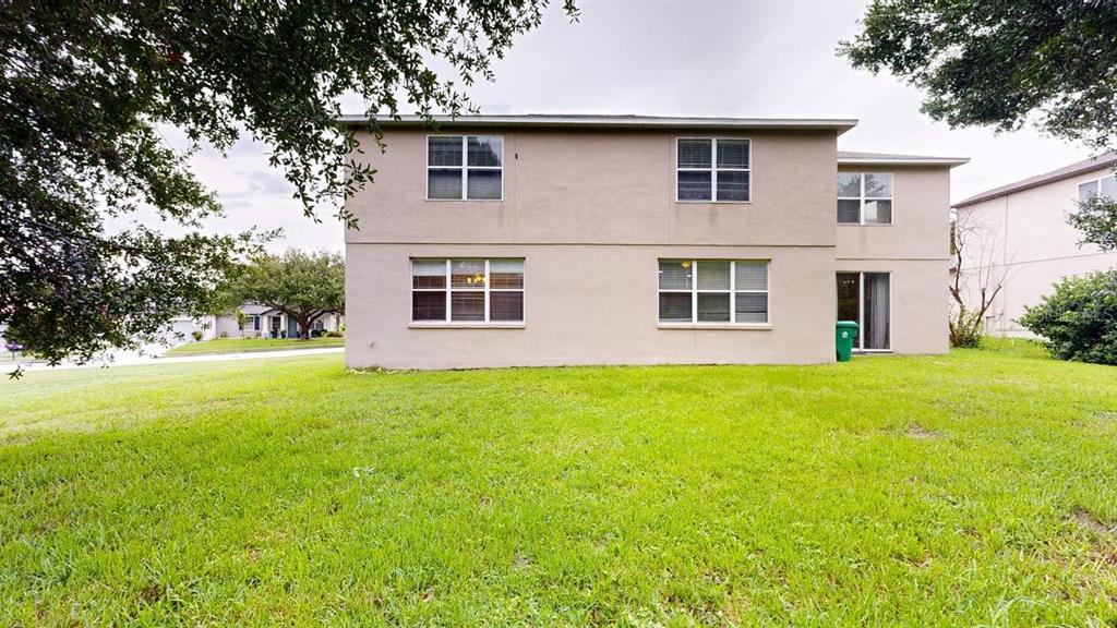 The rear exterior of a two-story beige house features a grassy yard and sliding glass doors — 14796 TULLAMORE LOOP, WINTER GARDEN, FL