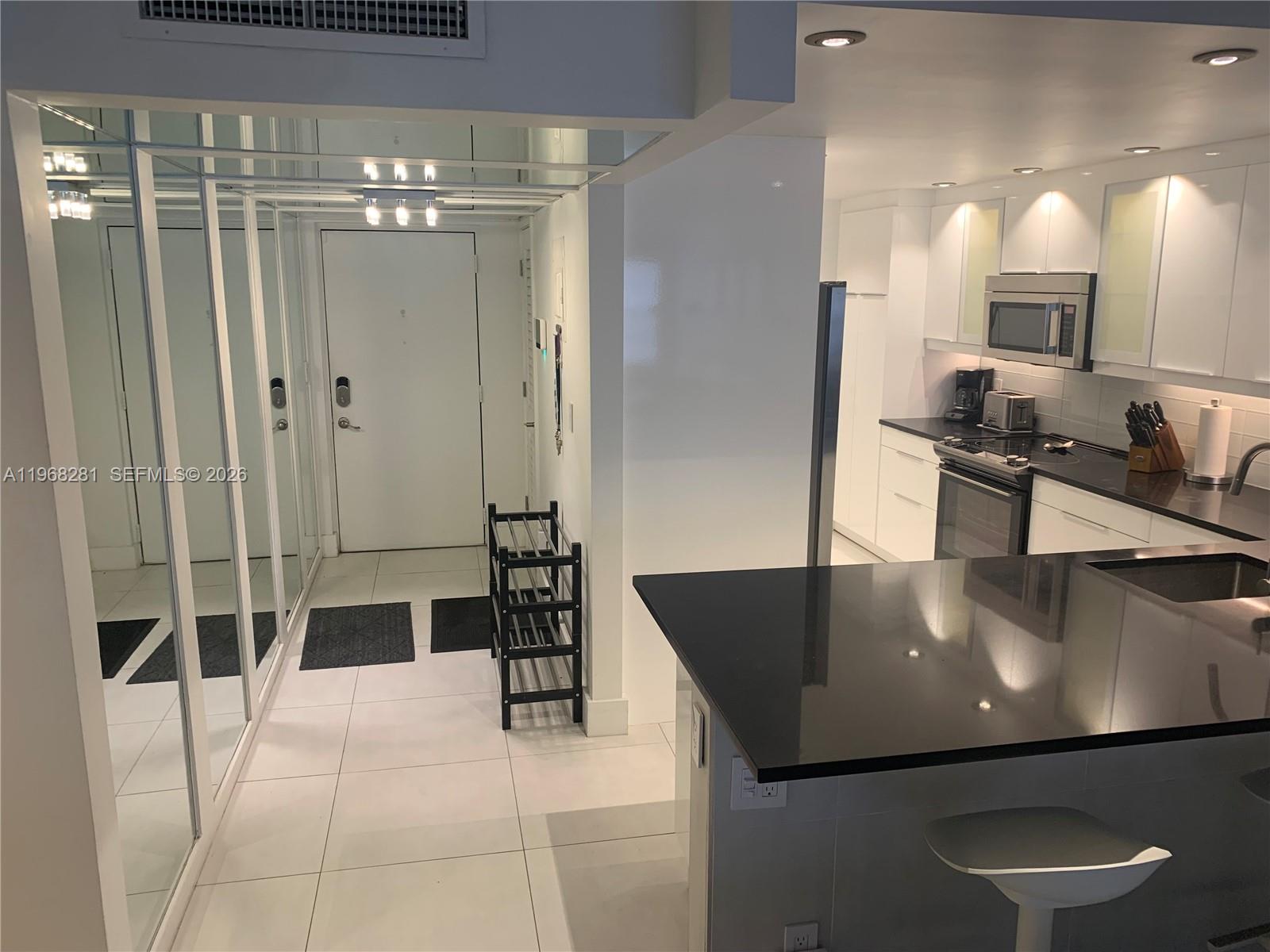 A kitchen with black countertops and white cabinets opens to a tiled entryway with mirrors — 2326 S Cypress Bend Dr # 221, Pompano Beach FL 33069, POMPANO BEACH, FL