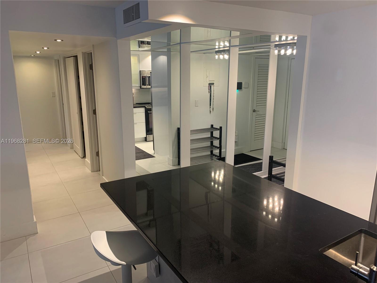 A kitchen island with a black countertop overlooks a hallway and a mirrored entryway — 2326 S Cypress Bend Dr # 221, Pompano Beach FL 33069, POMPANO BEACH, FL