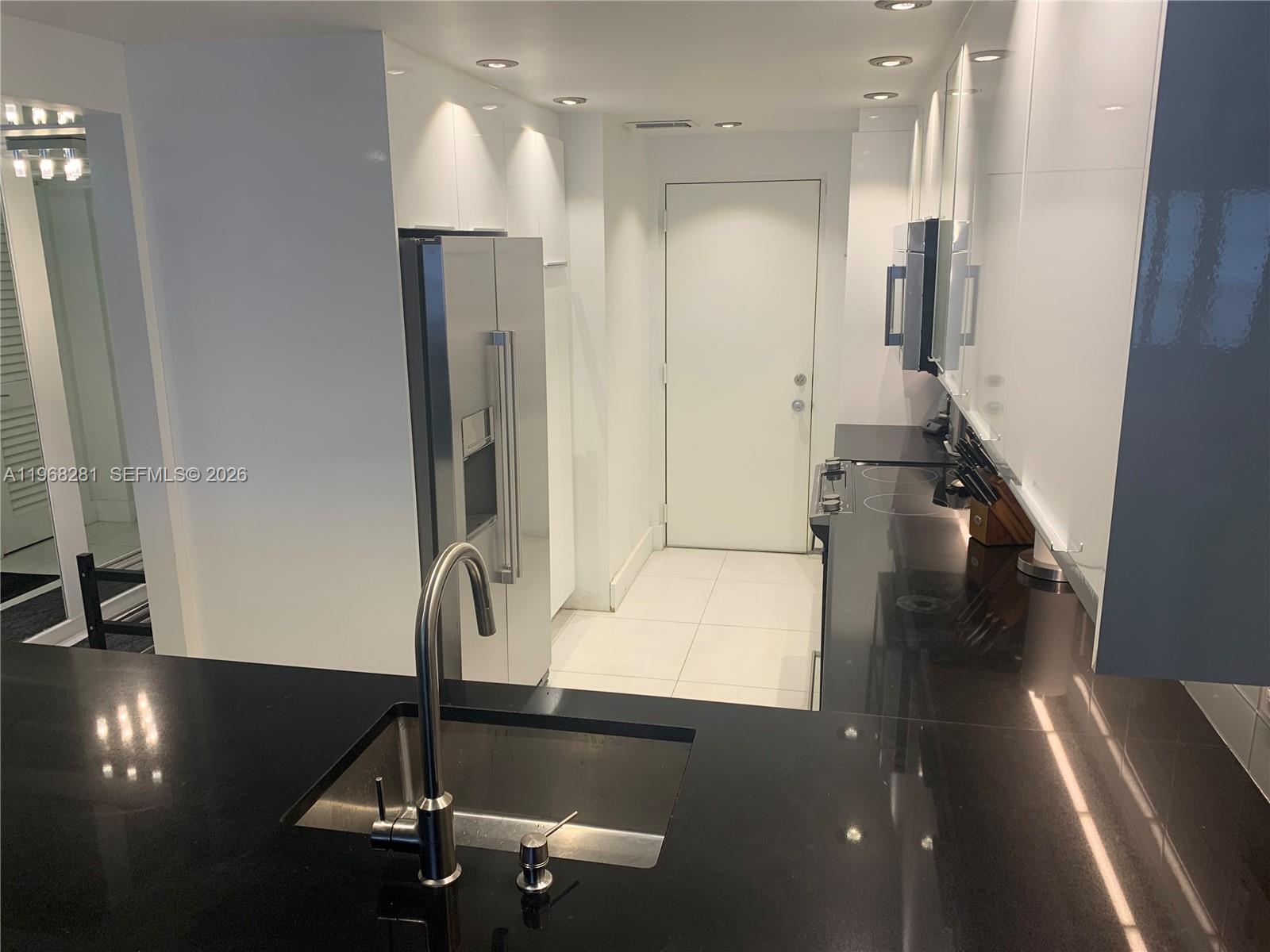 A modern kitchen features white cabinetry, black countertops, stainless steel appliances, and tile flooring — 2326 S Cypress Bend Dr # 221, Pompano Beach FL 33069, POMPANO BEACH, FL
