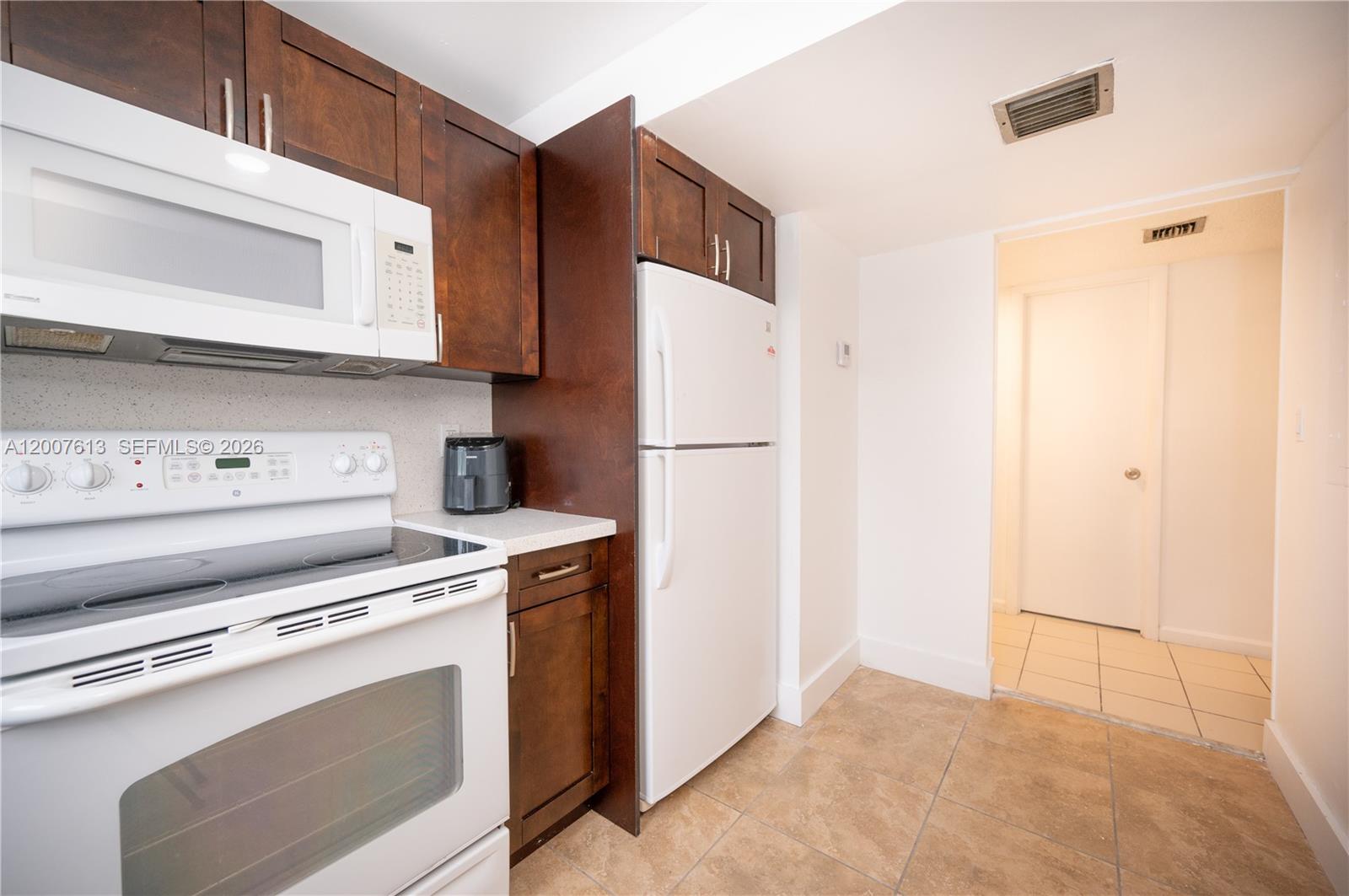 A kitchen features dark wood cabinets, white appliances, and light-colored tile flooring — 500 NE 26th St # 2C, Miami FL 33137, MIAMI, FL
