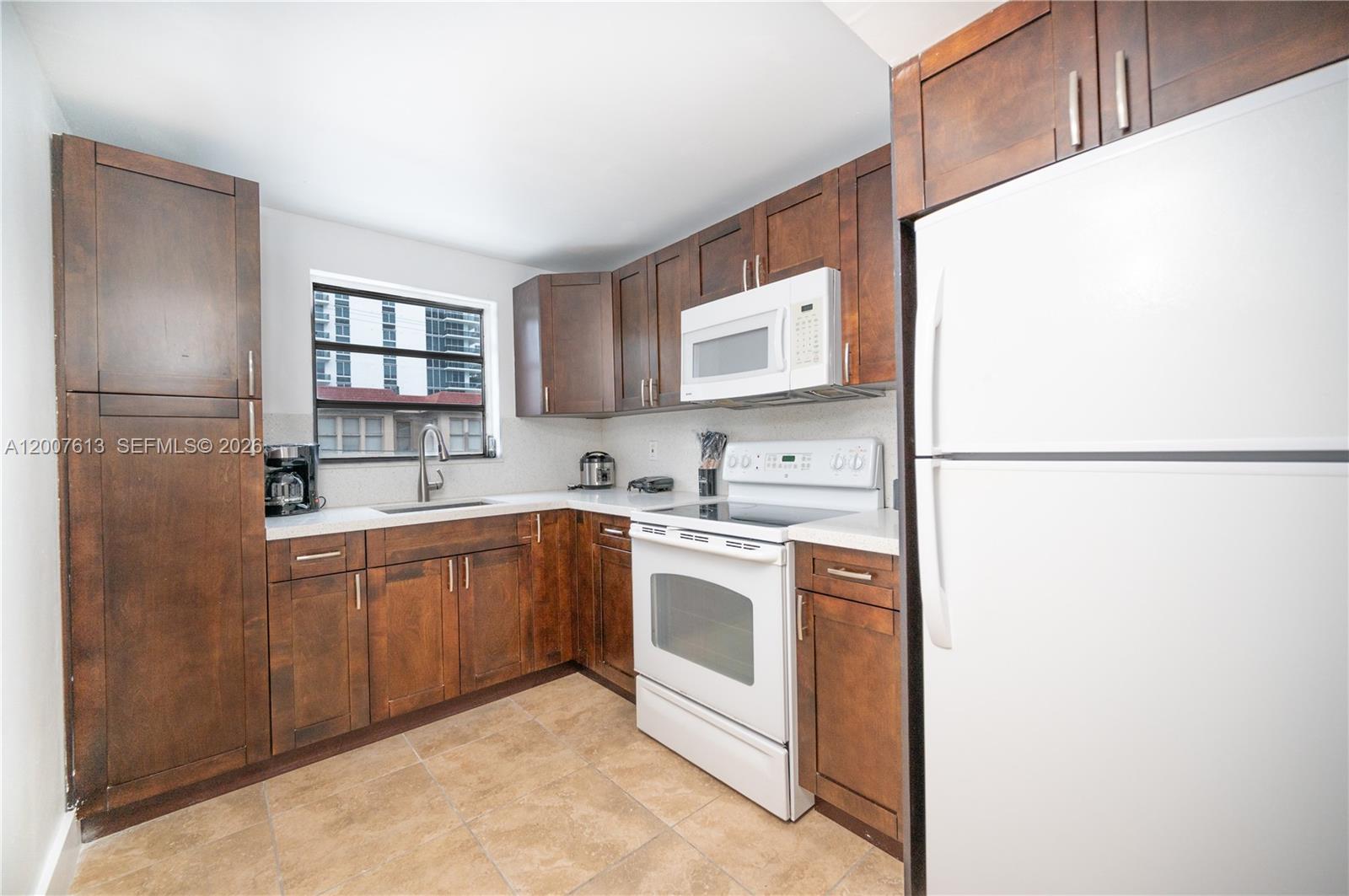 A kitchen features dark wood cabinets, white appliances, a window, and light-colored tile flooring — 500 NE 26th St # 2C, Miami FL 33137, MIAMI, FL
