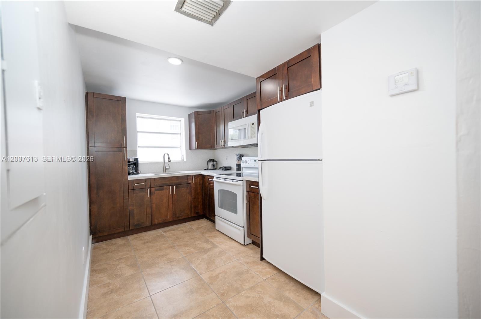 A kitchen features dark wood cabinetry, white appliances, and light-colored tile flooring — 500 NE 26th St # 2C, Miami FL 33137, MIAMI, FL