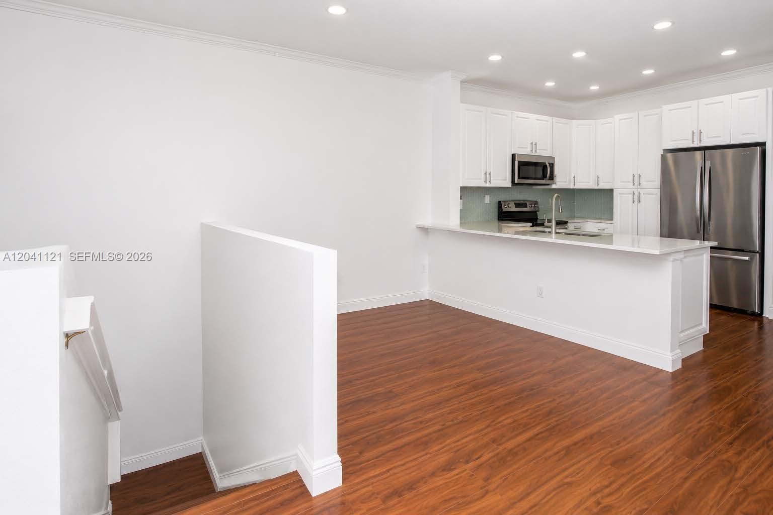 A kitchen with white cabinets and stainless steel appliances overlooks a room with wood flooring — 13127 SW 44th St # 12202, Miramar FL 33027, MIRAMAR, FL