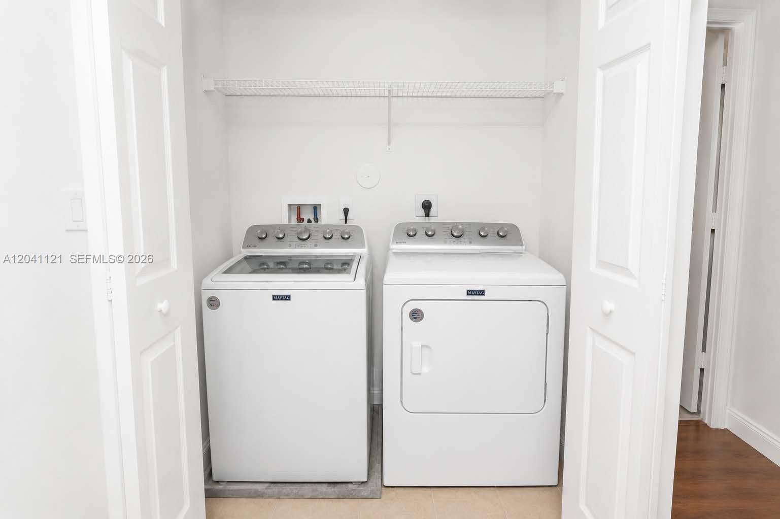 A laundry closet features a white top-load washer and dryer beneath a wire shelf — 13127 SW 44th St # 12202, Miramar FL 33027, MIRAMAR, FL