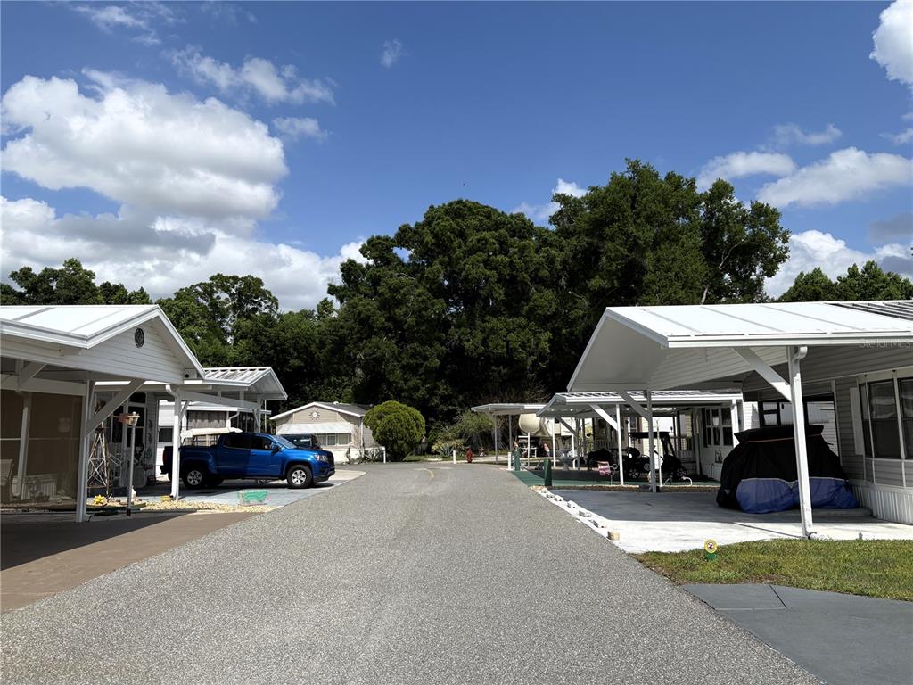 A paved street runs between two manufactured homes with covered carports under a blue sky — 446 CITRUS RIDGE, DAVENPORT, FL