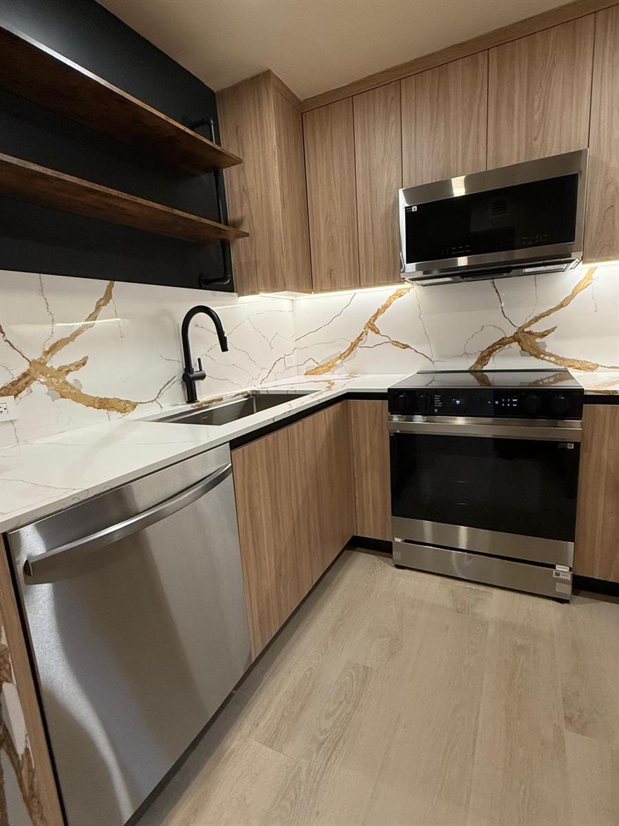 A modern kitchen features wood-grain cabinets, gold-veined white countertops, a stainless steel stove, and shelving — 7715 SW 86th Street # 111, Miami FL 33143, MIAMI, FL