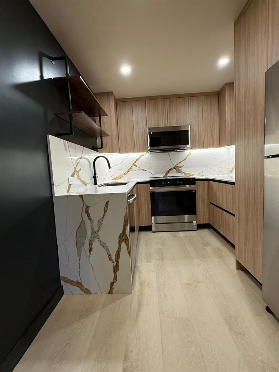 A modern kitchen features wood-grain cabinetry, gold-veined white quartz countertops, and a black accent wall — 7715 SW 86th Street # 111, Miami FL 33143, MIAMI, FL