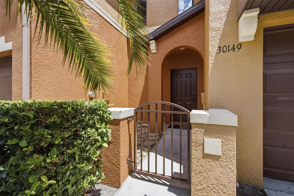 A gated entryway leads to a brown front door of a stucco townhouse — 30149 GOODWICK WAY, WESLEY CHAPEL, FL