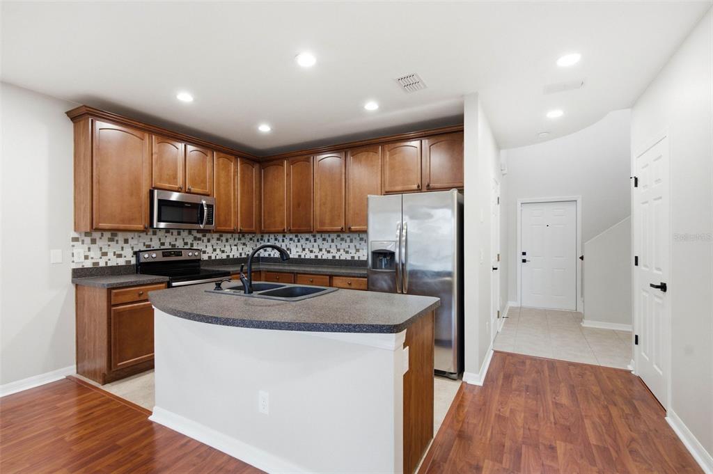A kitchen with wood cabinets, stainless steel appliances, a curved island, and a tile backsplash — 30149 GOODWICK WAY, WESLEY CHAPEL, FL