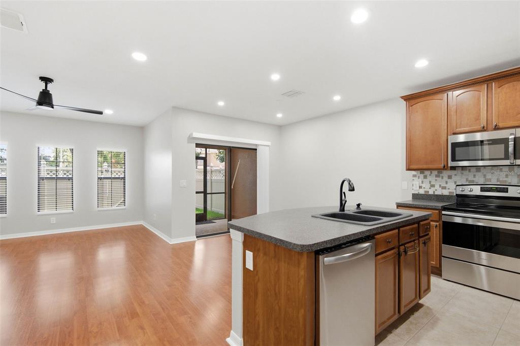 A kitchen with wood cabinets and a center island opens to a living area — 30149 GOODWICK WAY, WESLEY CHAPEL, FL
