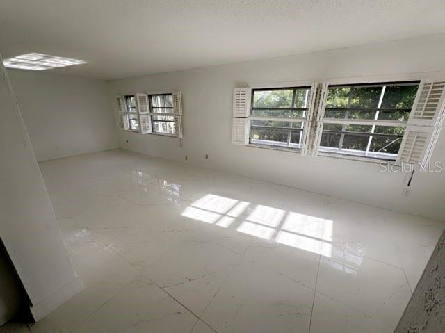An empty room features white marble-look tile flooring and windows with white plantation shutters — 9102 NW 81ST COURT, TAMARAC, FL