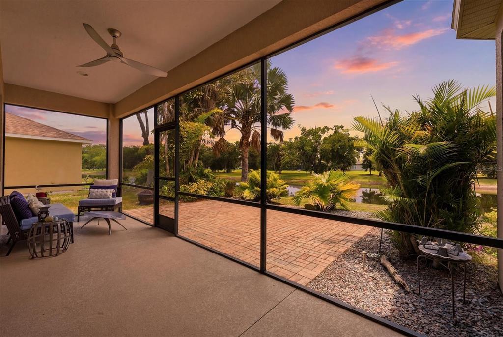A screened-in patio with outdoor furniture overlooks a brick paver terrace, palm trees, and water — 428 SNAPDRAGON LOOP, BRADENTON, FL