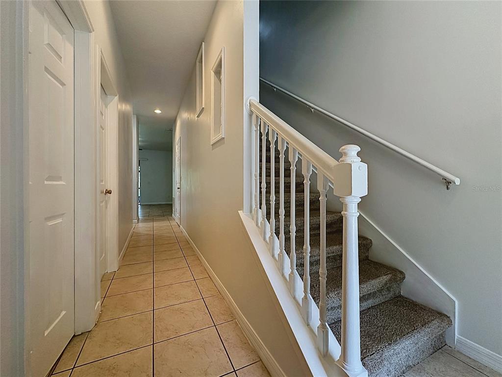A tiled hallway leads to a carpeted staircase with a white wooden railing — 2868 TANZANITE TER, KISSIMMEE, FL
