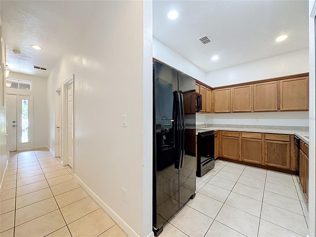 A kitchen with wood cabinets and black appliances sits adjacent to a tiled hallway — 2868 TANZANITE TER, KISSIMMEE, FL