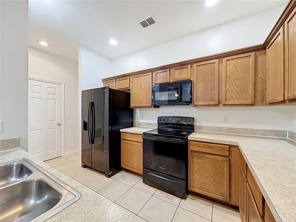 A kitchen features oak cabinets, black appliances, and light-colored countertops over tiled floors — 2868 TANZANITE TER, KISSIMMEE, FL