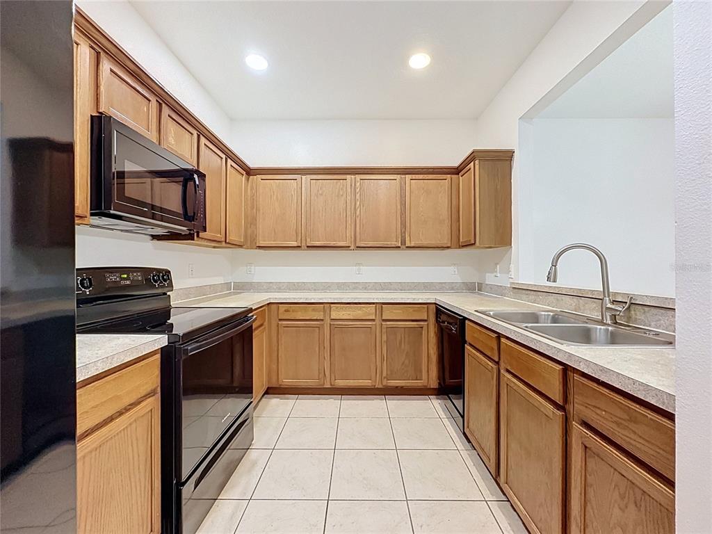 A kitchen features oak cabinets, black appliances, laminate countertops, and light-colored tile flooring — 2868 TANZANITE TER, KISSIMMEE, FL