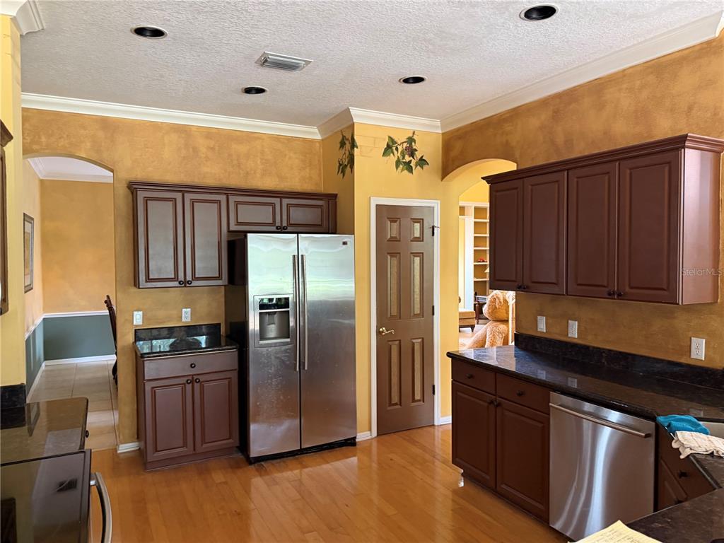 A kitchen features dark wood cabinets, stainless steel appliances, granite countertops, and yellow textured walls — 18826 AVENUE BIARRITZ, LUTZ, FL