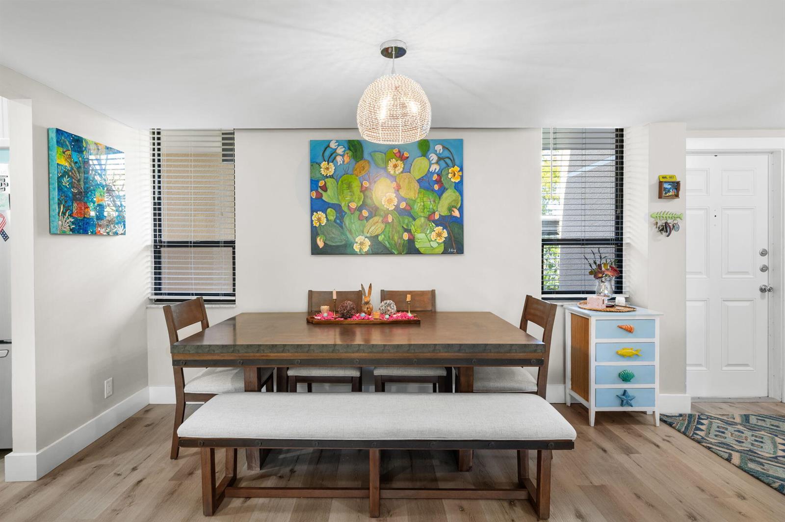 A dining room features a wooden table with a bench, chairs, and a floral painting — 3412 NE Causeway Boulevard # 102, Jensen Beach FL 34957, JENSEN BEACH, FL