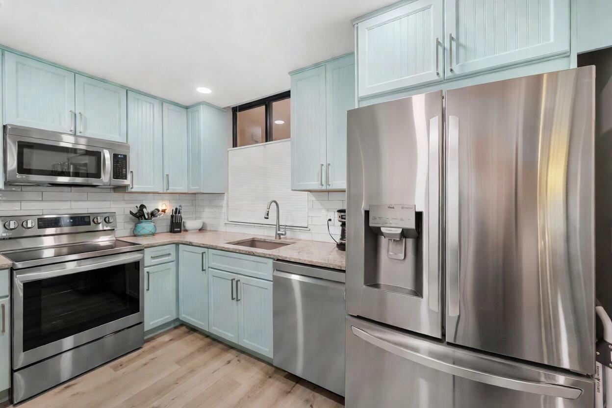 A kitchen with light blue cabinets, stainless steel appliances, and light wood-look flooring — 3412 NE Causeway Boulevard # 102, Jensen Beach FL 34957, JENSEN BEACH, FL