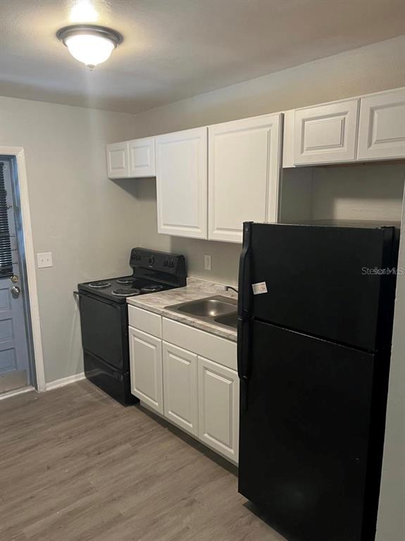 A kitchen features white cabinets, a black stove, a black refrigerator, and wood-look flooring — 8123 N ALASKA STREET UNIT A, TAMPA, FL